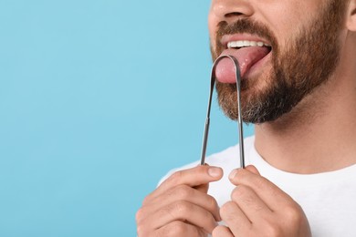 Photo of Man brushing his tongue with cleaner on light blue background, closeup. Space for text