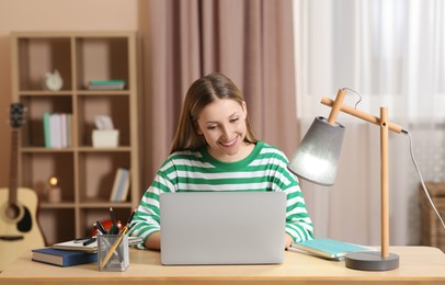 Photo of Online learning. Smiling teenage girl typing on laptop at home