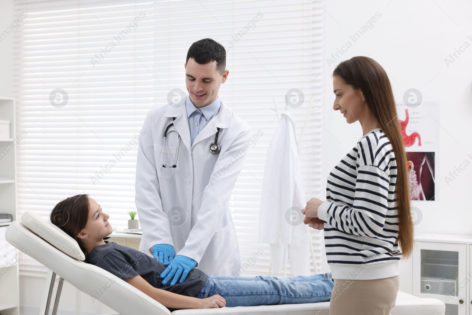 Photo of Gastroenterologist examining girl with stomach ache on couch in clinic