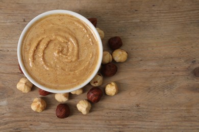 Photo of Delicious nut butter in bowl and hazelnuts on wooden table, top view. Space for text