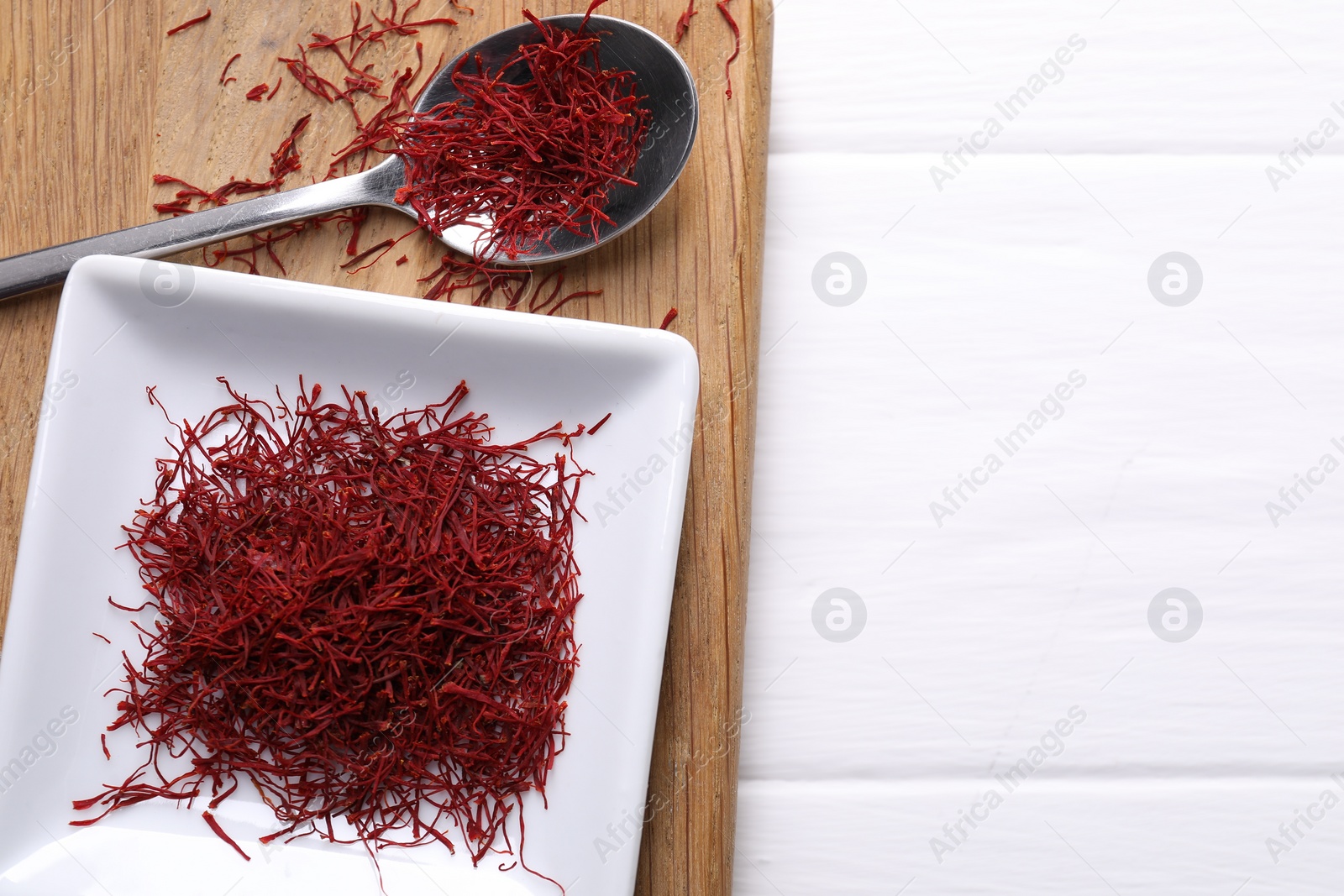 Photo of Aromatic saffron and spoon on white wooden table, top view. Space for text