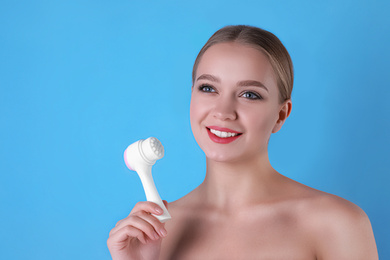 Young woman with face cleansing brush on light blue background. Cosmetic product