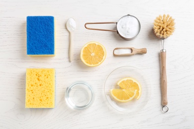 Photo of Baking soda, vinegar, lemon, cleaning brush and sponges on white wooden table, flat lay