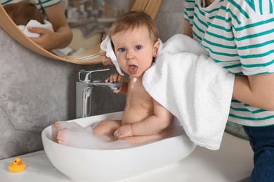 Photo of Mother washing her little baby in sink at home