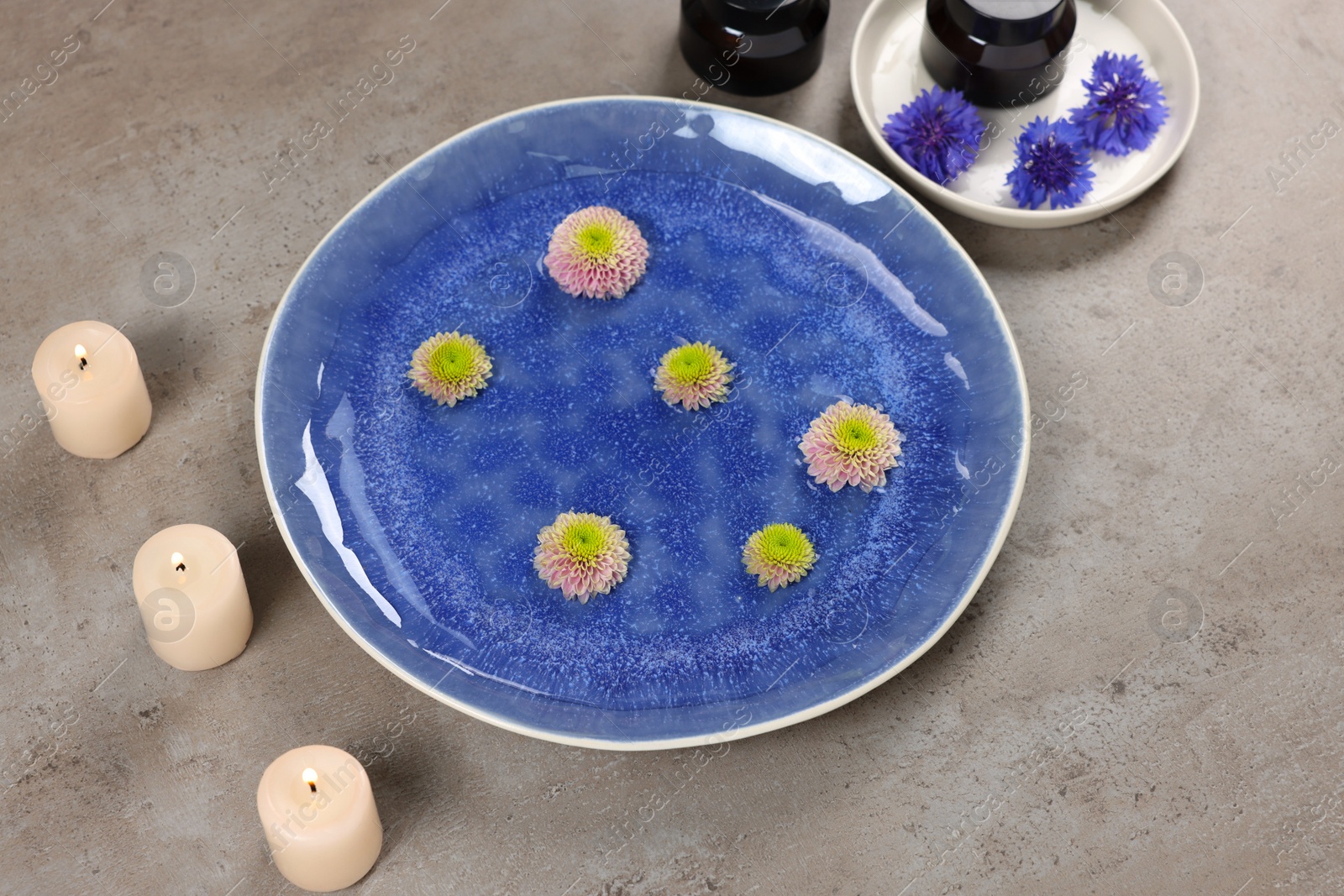 Photo of Plate with water, flowers and burning candles on grey floor. Pedicure procedure