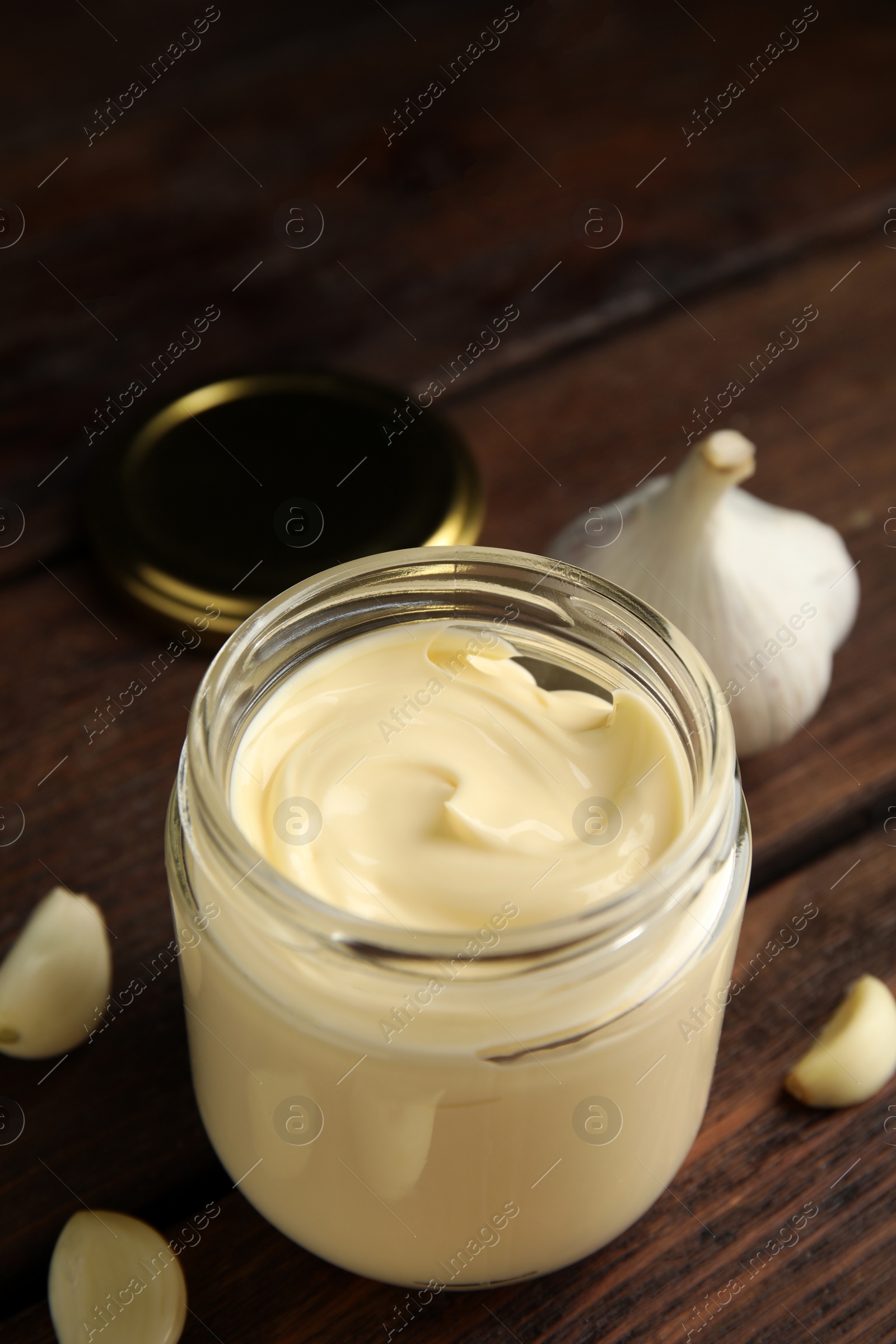 Photo of Jar of delicious mayonnaise and fresh garlic on wooden table