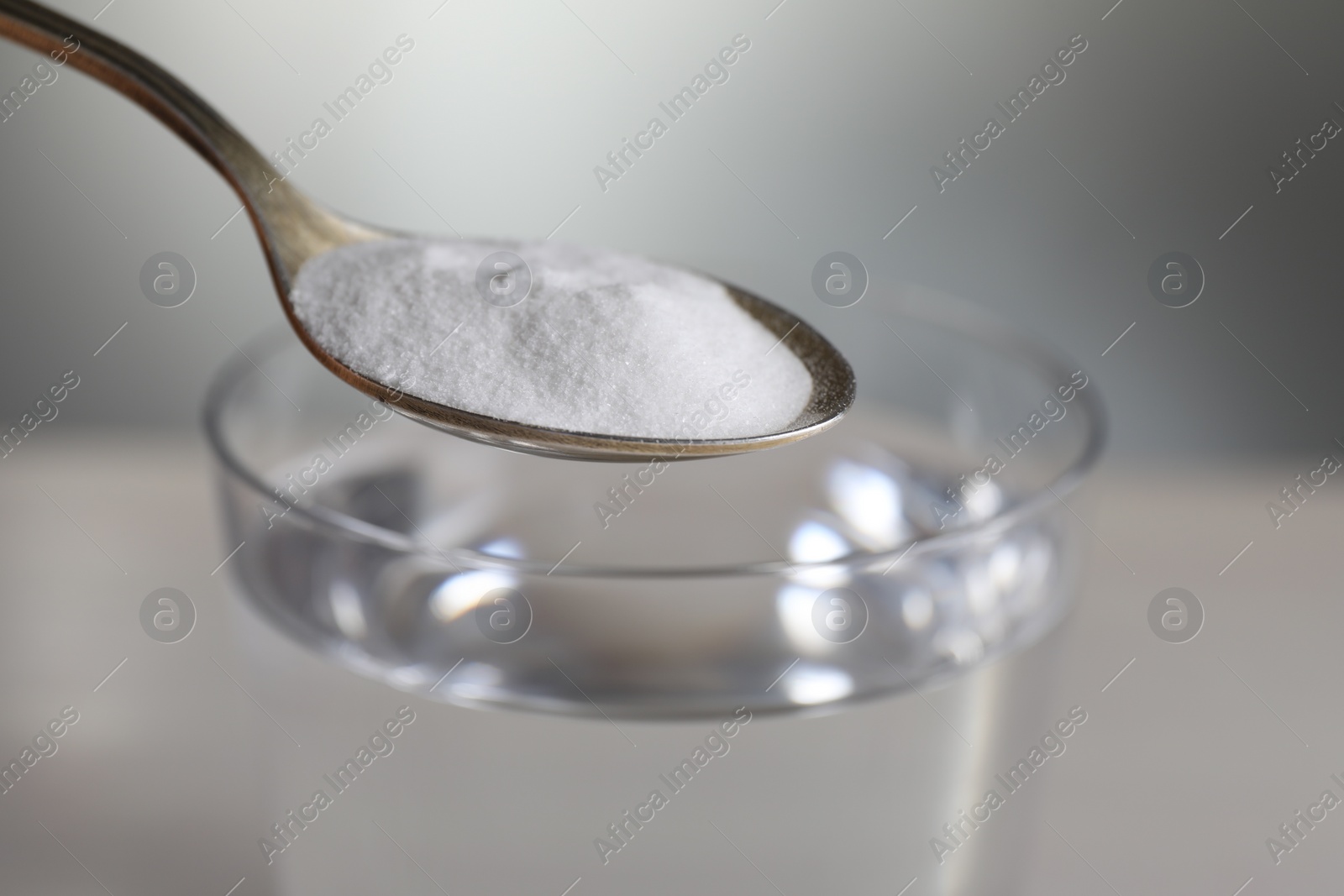 Photo of Spoon with baking soda over glass of water on light grey background, closeup