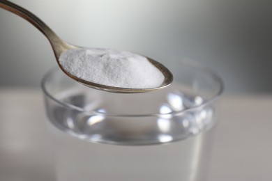 Photo of Spoon with baking soda over glass of water on light grey background, closeup