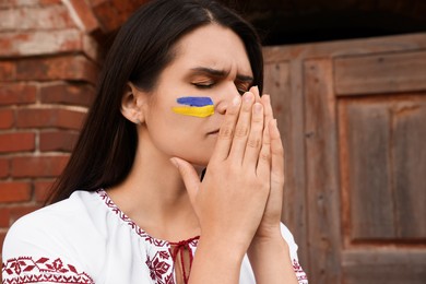 Photo of Sad young woman with drawing of Ukrainian flag on face outdoors, space for text