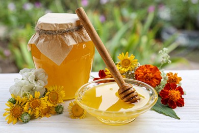Photo of Delicious honey and dipper with different flowers on white wooden table in garden