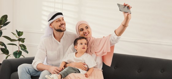 Happy Muslim family taking selfie on sofa at home. Banner design 