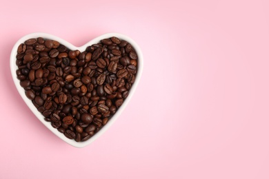 Heart shaped bowl with coffee beans on color background, top view with space for text