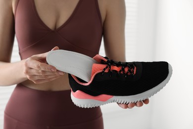 Photo of Sporty woman putting orthopedic insole into shoe on blurred background, closeup. Foot care