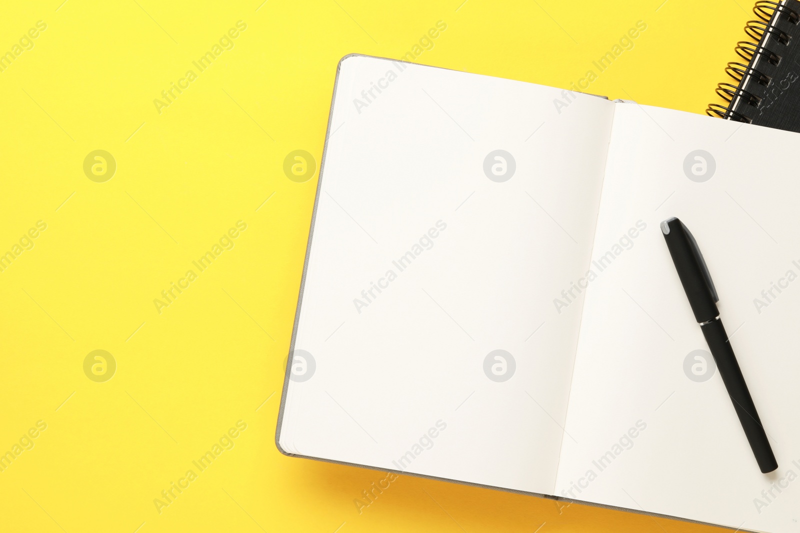 Photo of Notebooks and pen on yellow background, top view. Space for text