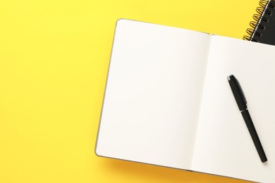 Photo of Notebooks and pen on yellow background, top view. Space for text