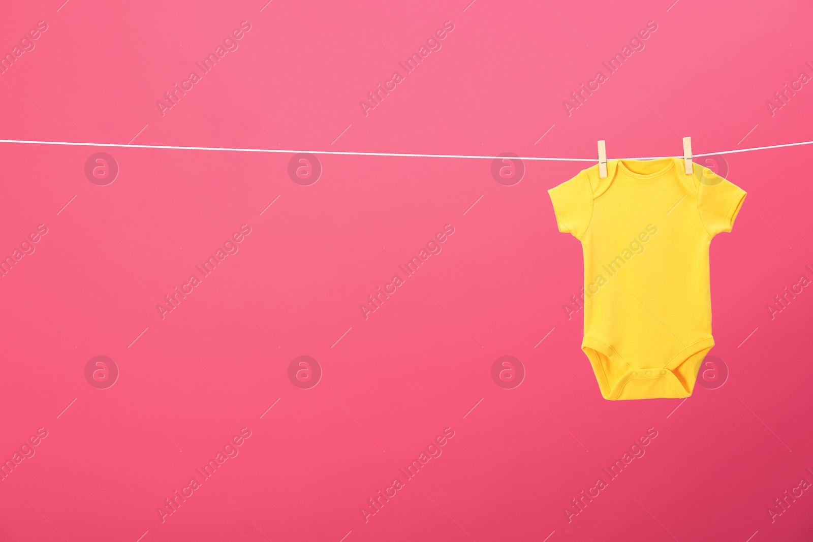 Photo of Baby onesie hanging on clothes line against pink background, space for text