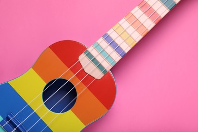Colorful ukulele on pink background, top view. String musical instrument