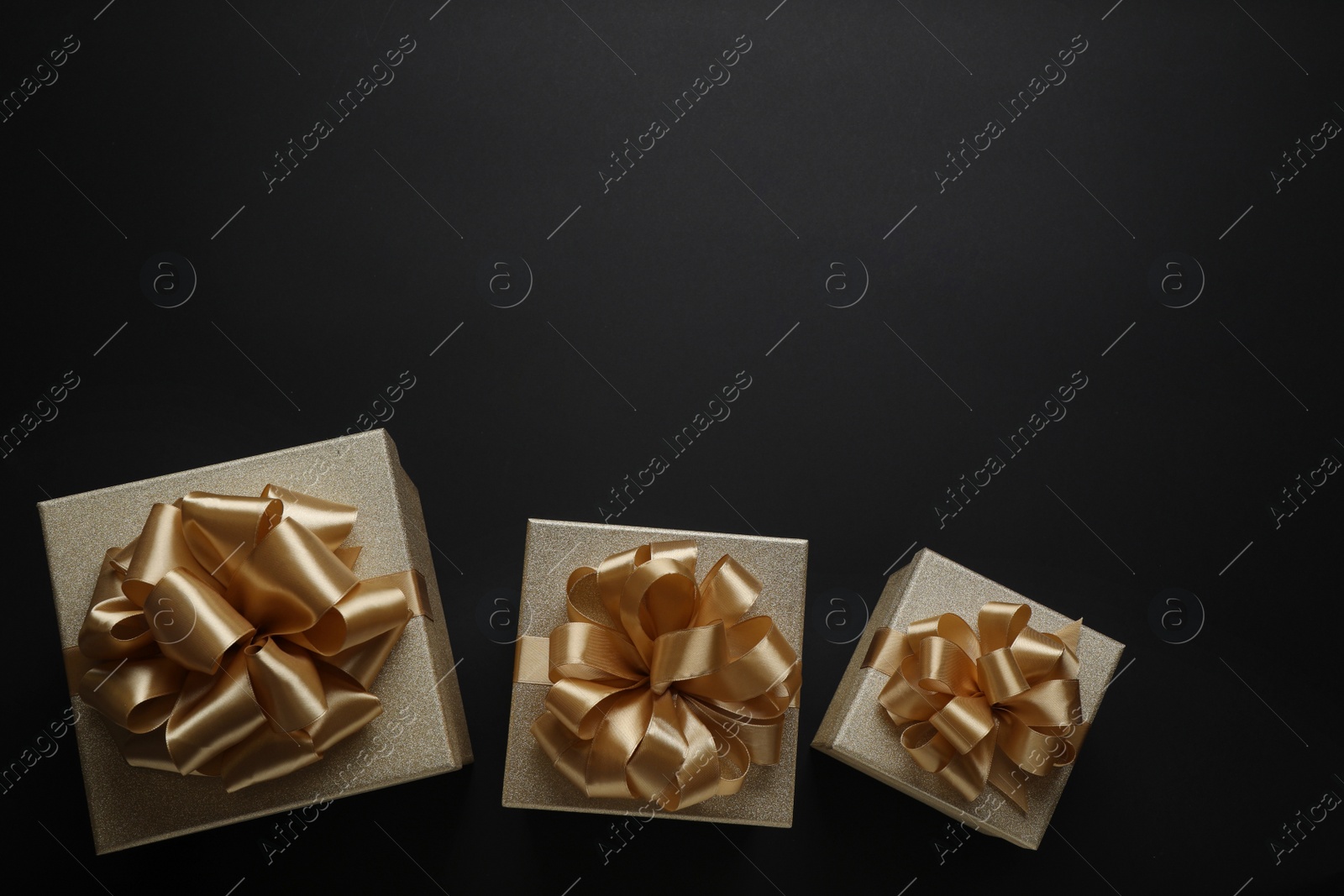 Photo of Golden gift boxes on black background, flat lay. Space for text
