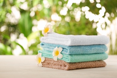 Photo of Pile of fresh towels and flowers on table against blurred background, space for text