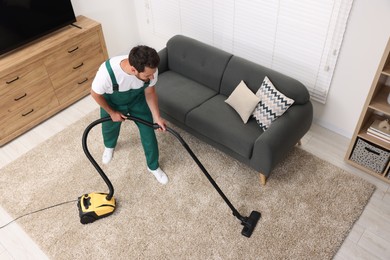Photo of Dry cleaner's employee hoovering carpet with vacuum cleaner in room, above view