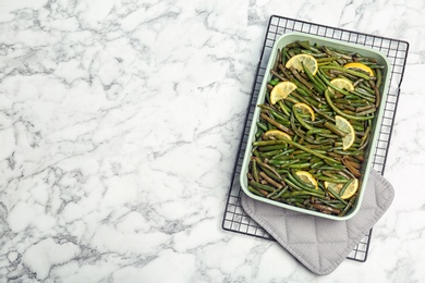 Photo of Dish with tasty green beans and lemons on marble table, top view