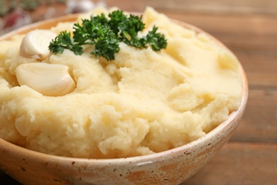 Photo of Tasty mashed potatoes served with parsley and garlic in bowl, closeup