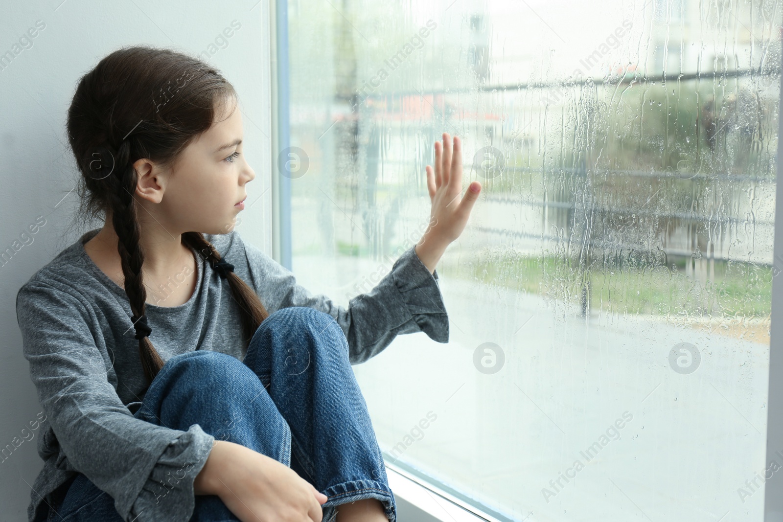 Photo of Sad little girl near window indoors on rainy day