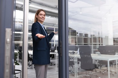 Happy real estate agent in suit inviting inside