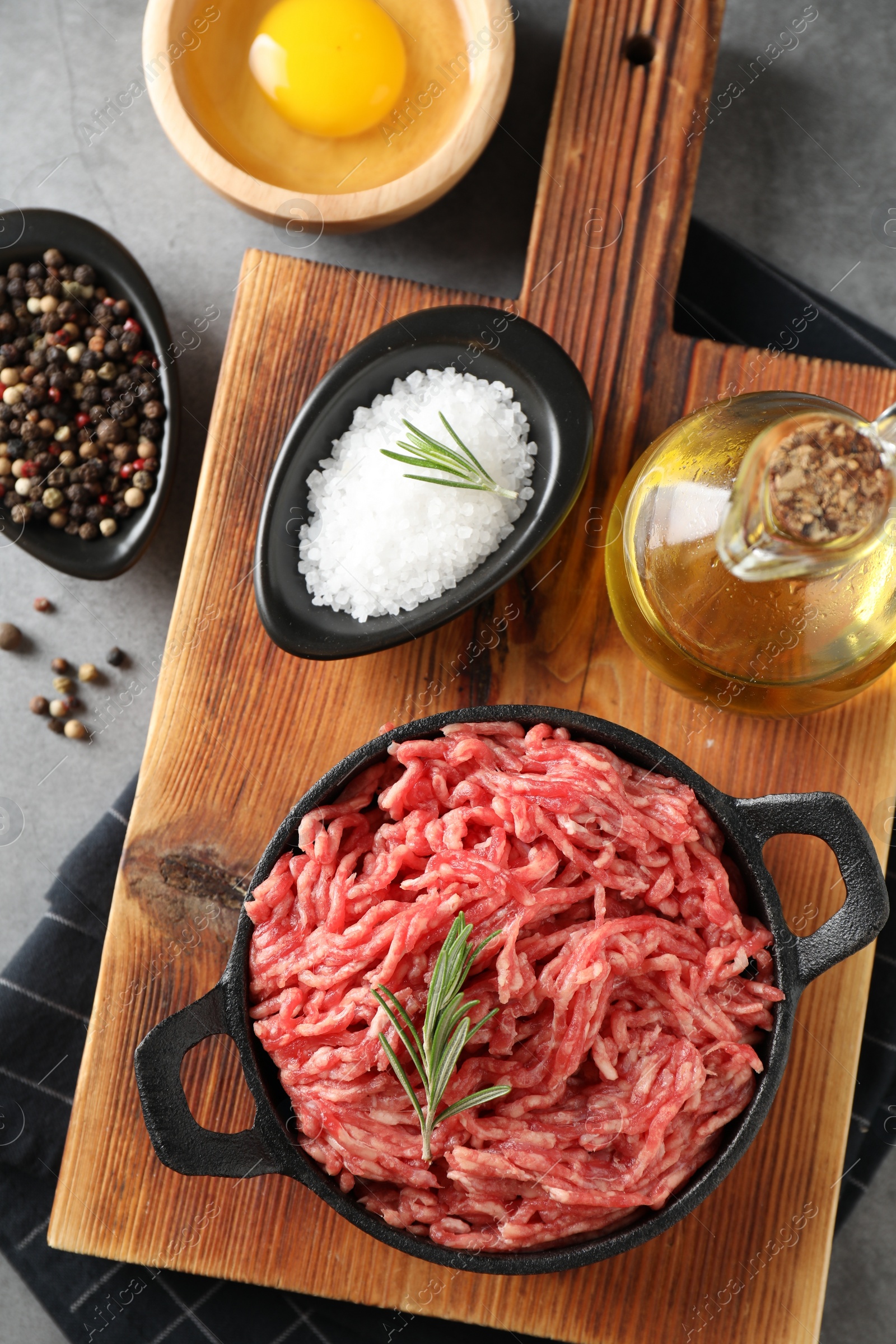 Photo of Raw ground meat in bowl, spices, egg and oil on grey table, flat lay