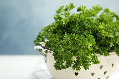 Photo of Colander with fresh green parsley against color background, closeup