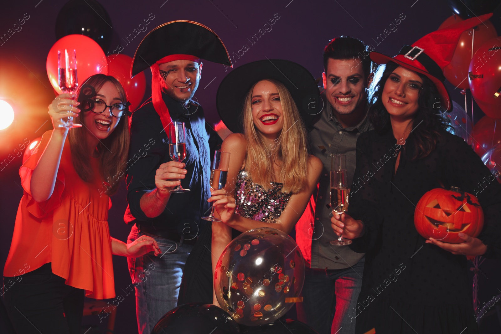 Photo of Happy friends in costumes enjoying Halloween party on dark background