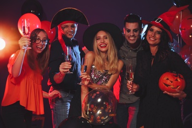 Happy friends in costumes enjoying Halloween party on dark background