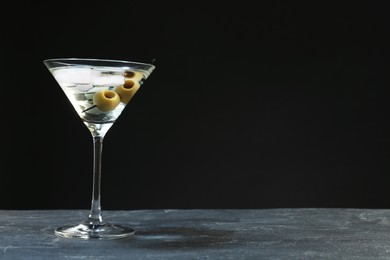 Martini cocktail with ice and olives on grey table against dark background. Space for text