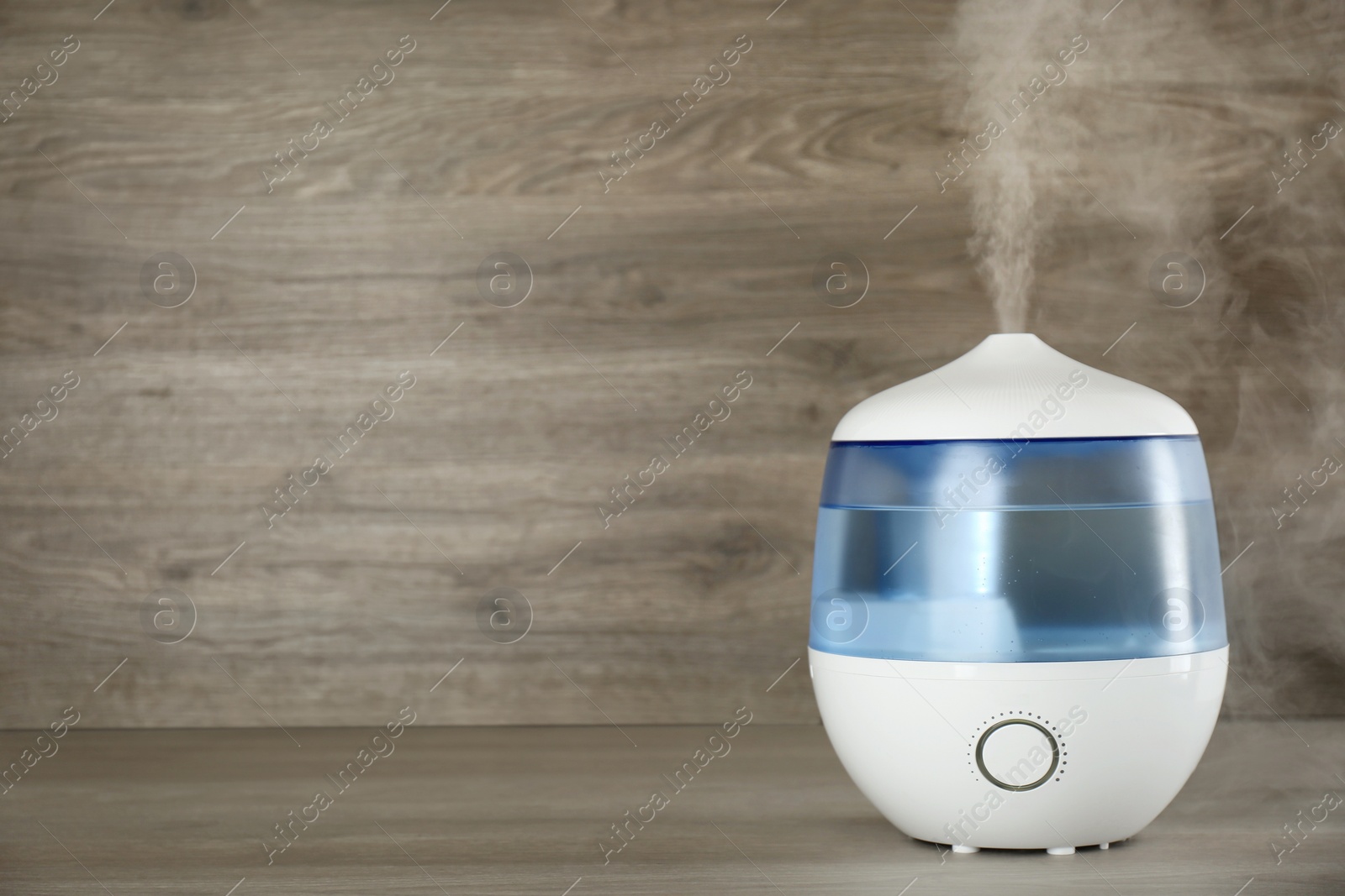 Photo of Modern air humidifier on wooden table. Space for text