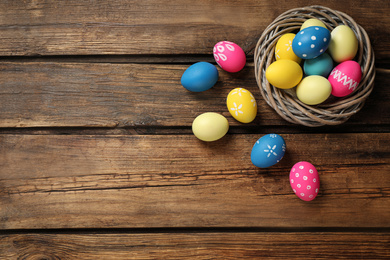 Photo of Colorful Easter eggs in decorative nest on wooden background, flat lay. Space for text