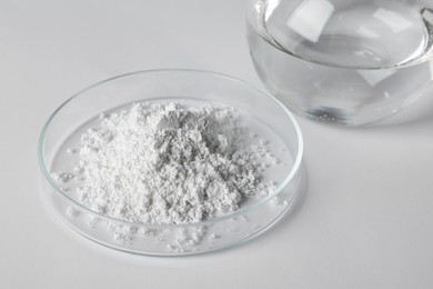 Photo of Petri dish with calcium carbonate powder and laboratory flask on white table
