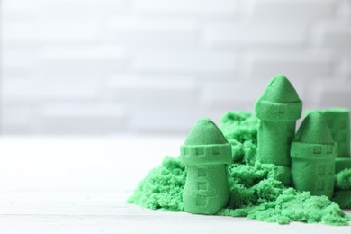 Photo of Castle figures made of green kinetic sand on white table, closeup. Space for text