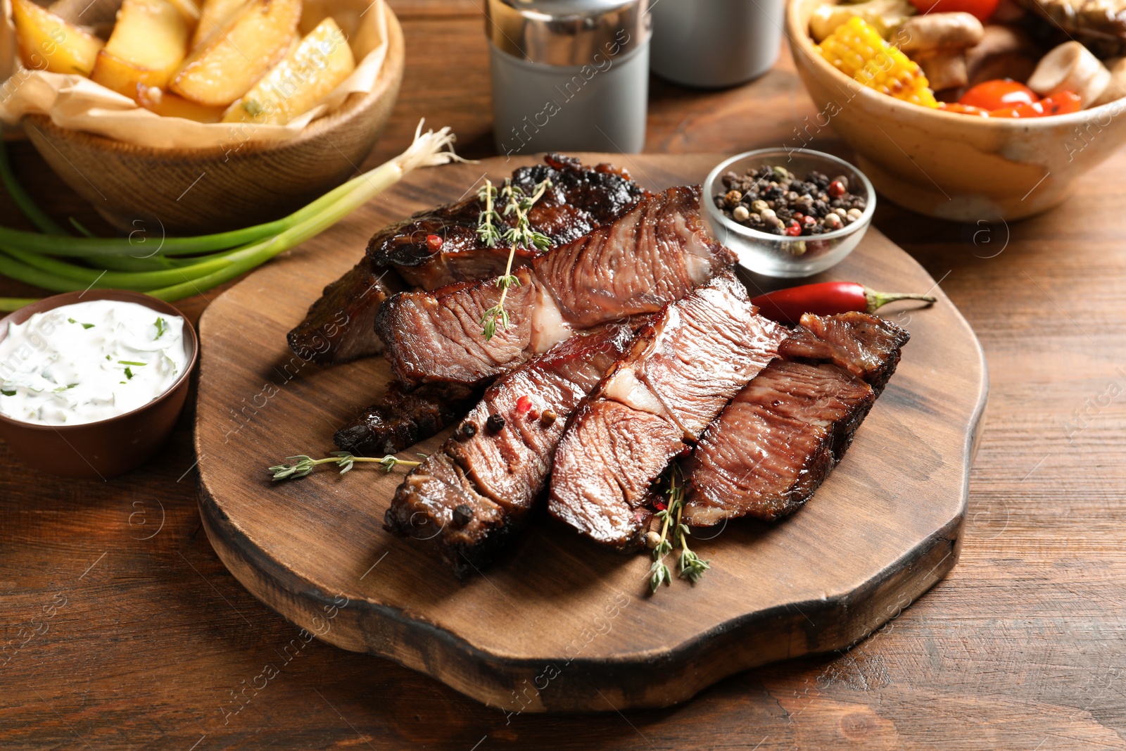 Photo of Serving board with delicious barbecued steak and spices on wooden table