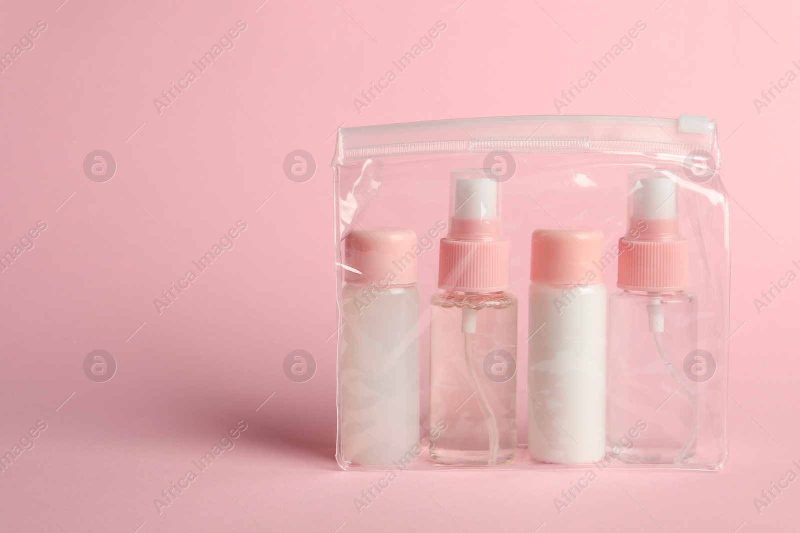 Photo of Cosmetic travel kit in plastic bag on pink background. Space for text