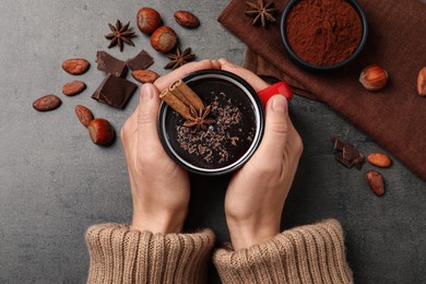 Woman with mug of yummy hot chocolate at grey table, top view