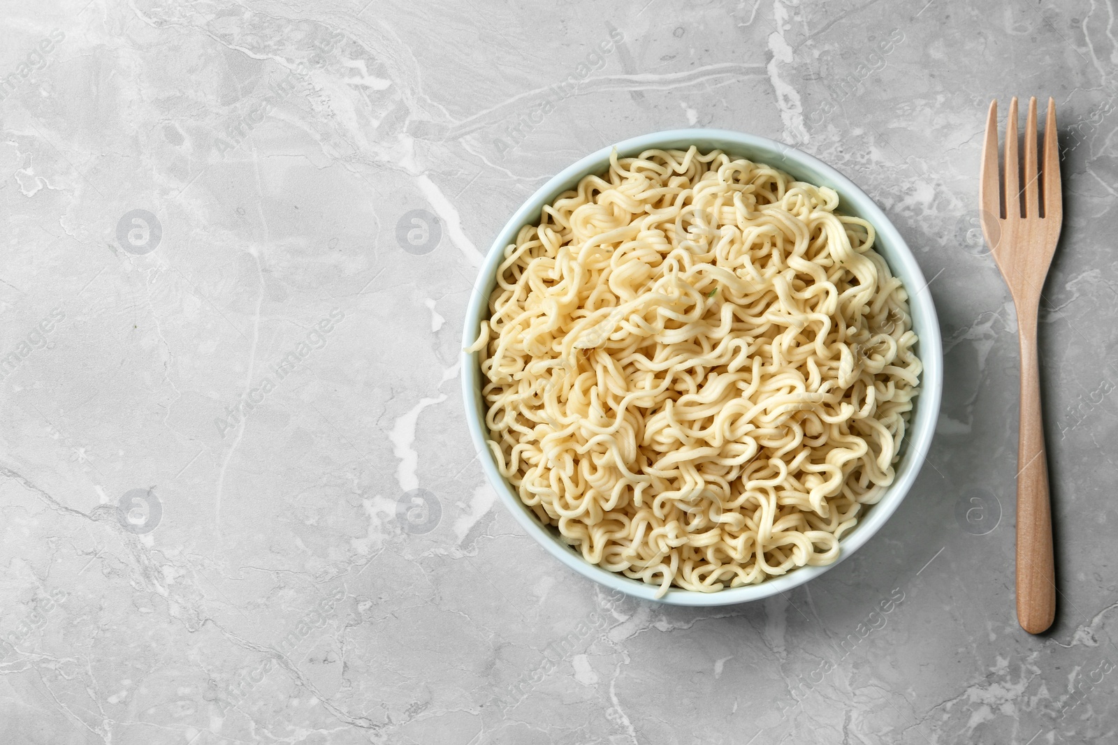 Photo of Bowl of tasty noodles with fork served on table, flat lay. Space for text