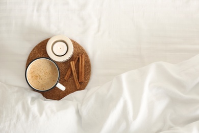 Cup of aromatic coffee, cinnamon sticks and candle on bed with soft blanket, top view. Space for text