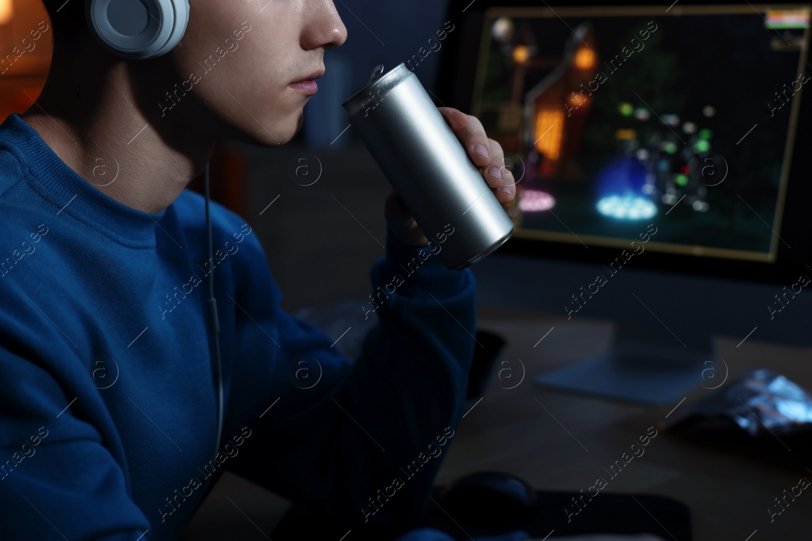 Photo of Young man with energy drink playing video game at wooden desk indoors, closeup