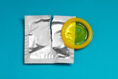 Torn condom package on light blue background, top view. Safe sex