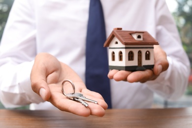 Photo of Real estate agent holding house model and keys at table