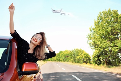 Young woman leaning out of car window and airplane in sky. Summer vacation