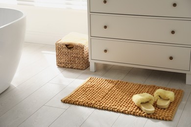 Photo of Stylish orange mat with slippers near chest of drawers in bathroom