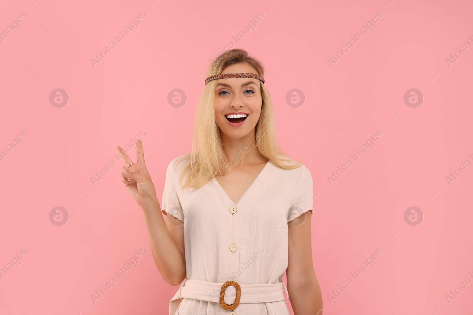 Photo of Portrait of happy hippie woman showing peace sign on pink background