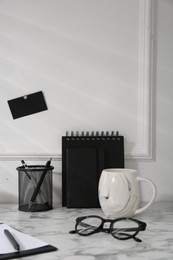 Stylish office workplace. Decor elements, glasses, cup and stationery on marble table near white wall