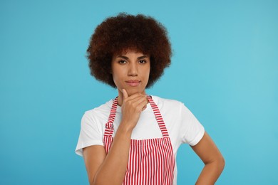 Photo of Thoughtful young woman in apron on light blue background